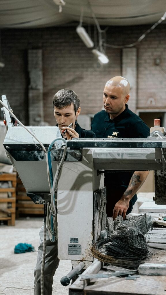 Two men operate machinery in a workshop, focused on their task.